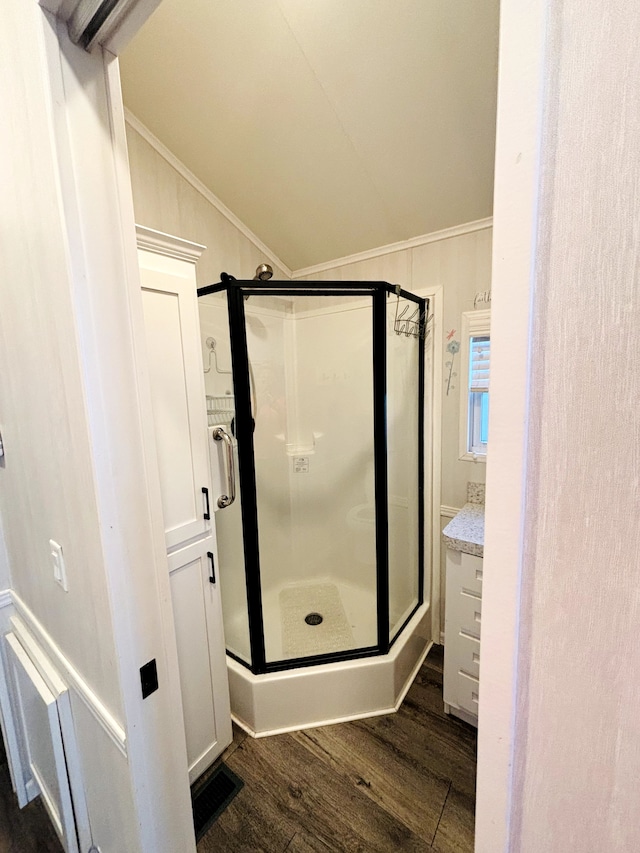 bathroom with a shower with door, ornamental molding, vaulted ceiling, and hardwood / wood-style flooring