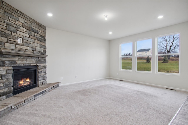 unfurnished living room featuring a stone fireplace and light carpet