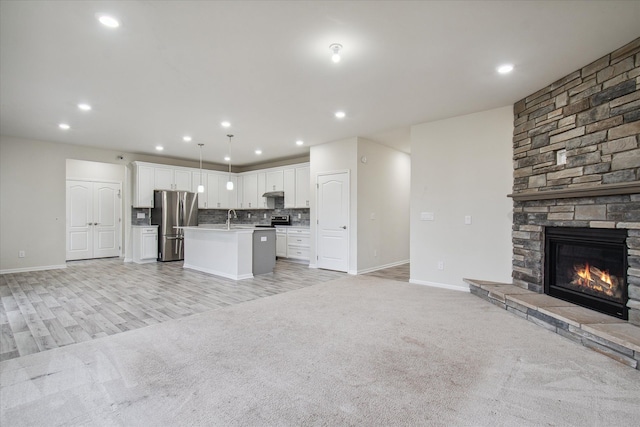 kitchen featuring a center island with sink, white cabinets, hanging light fixtures, a fireplace, and stainless steel appliances