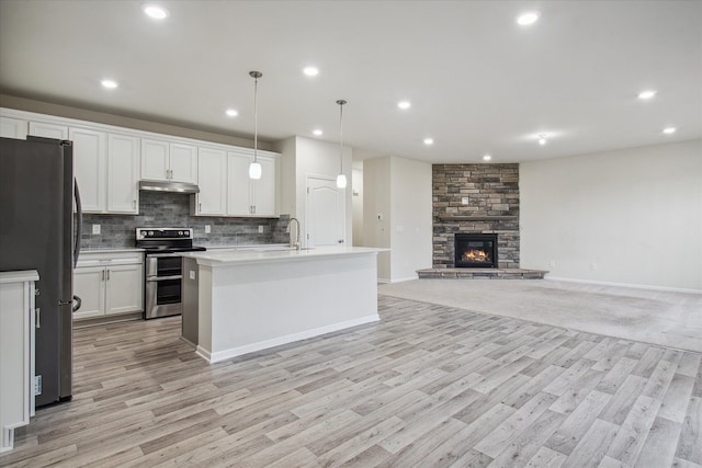 kitchen with pendant lighting, white cabinets, a stone fireplace, light hardwood / wood-style flooring, and stainless steel appliances