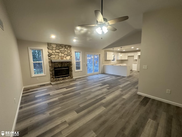 unfurnished living room with lofted ceiling, dark wood-type flooring, a stone fireplace, and ceiling fan