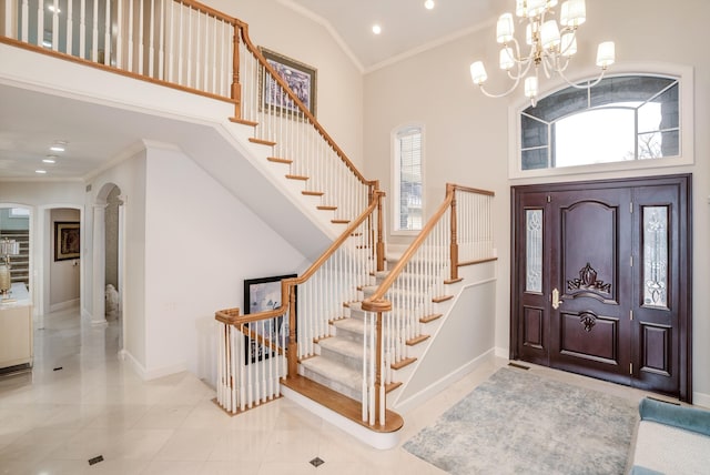 tiled foyer with crown molding, a notable chandelier, plenty of natural light, and a high ceiling