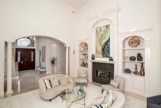 living room with a high ceiling, built in features, ornamental molding, a notable chandelier, and decorative columns