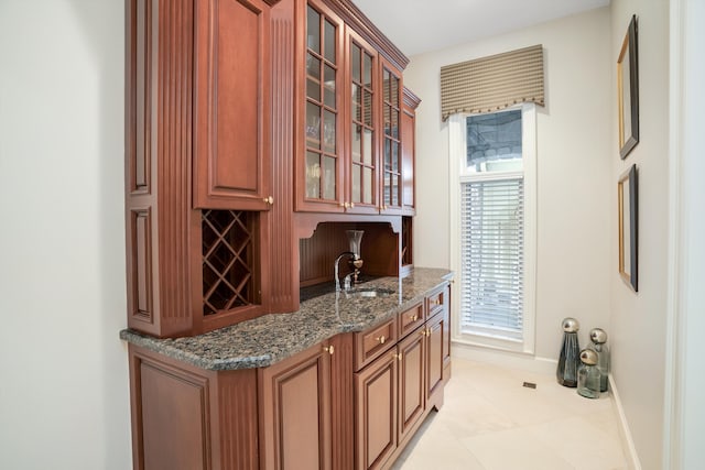 bar with light tile patterned flooring, dark stone countertops, and sink