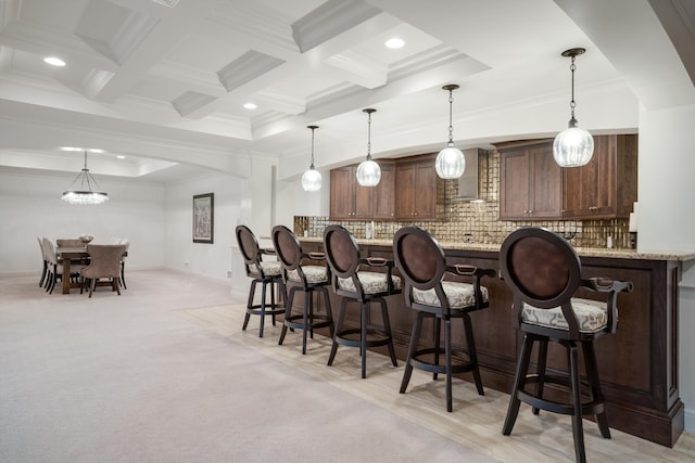 bar with decorative light fixtures, wall chimney range hood, tasteful backsplash, light stone counters, and light colored carpet