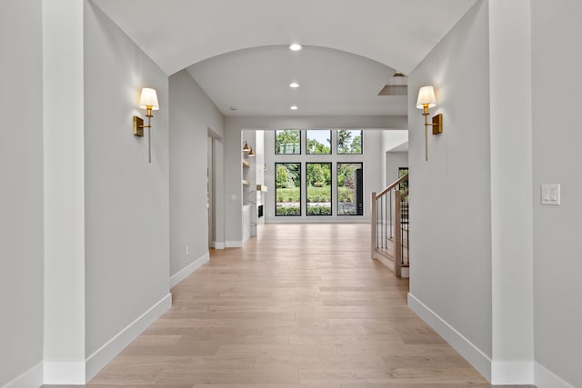 hallway featuring light wood-style flooring, baseboards, arched walkways, stairs, and recessed lighting