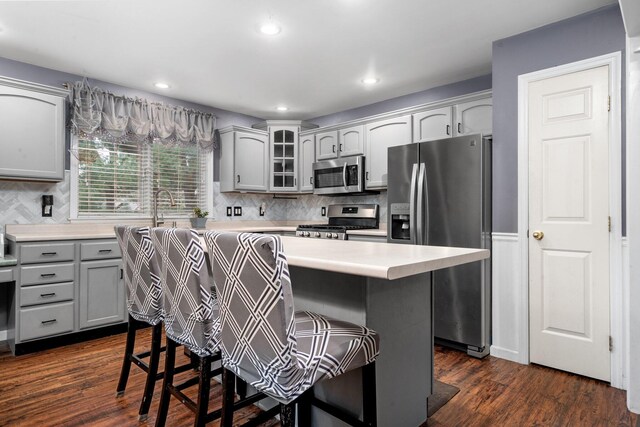 kitchen with a kitchen bar, appliances with stainless steel finishes, gray cabinetry, a center island, and dark hardwood / wood-style floors