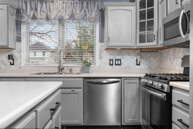 kitchen with decorative backsplash, appliances with stainless steel finishes, gray cabinets, and sink