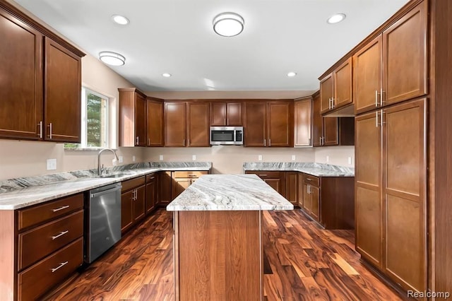 kitchen with appliances with stainless steel finishes, a center island, light stone counters, and dark hardwood / wood-style flooring