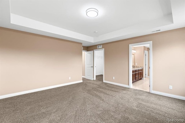 unfurnished bedroom with light carpet, ensuite bathroom, and a raised ceiling