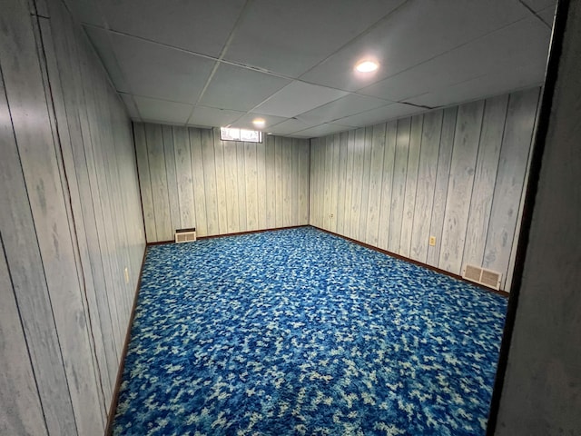 basement featuring carpet flooring, a paneled ceiling, and wood walls