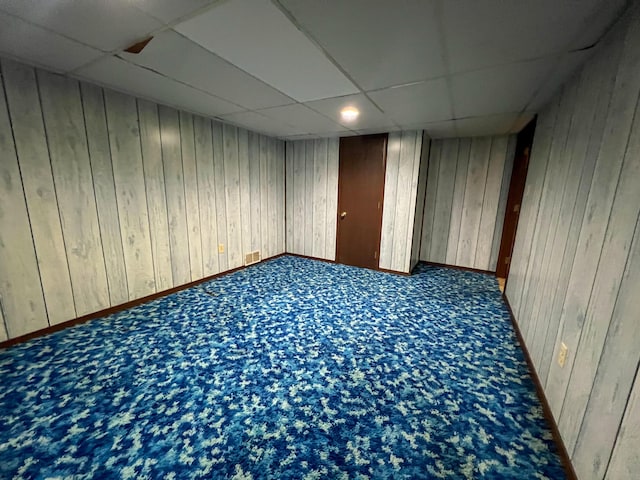 basement featuring carpet flooring, a paneled ceiling, and wooden walls