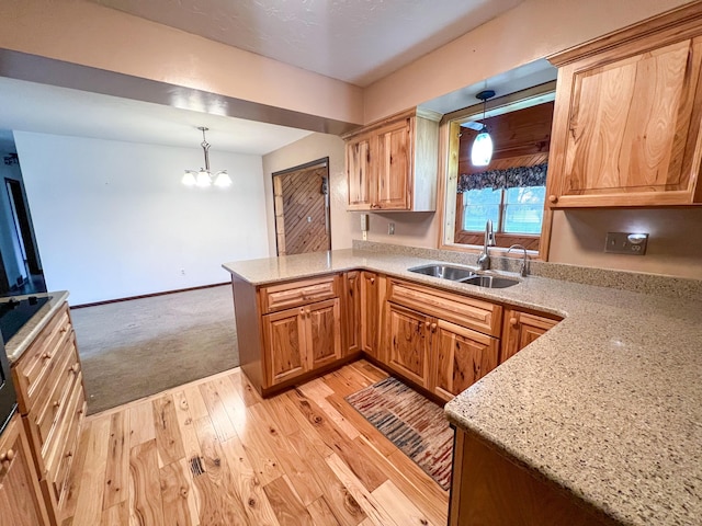 kitchen with kitchen peninsula, light stone counters, sink, pendant lighting, and a notable chandelier