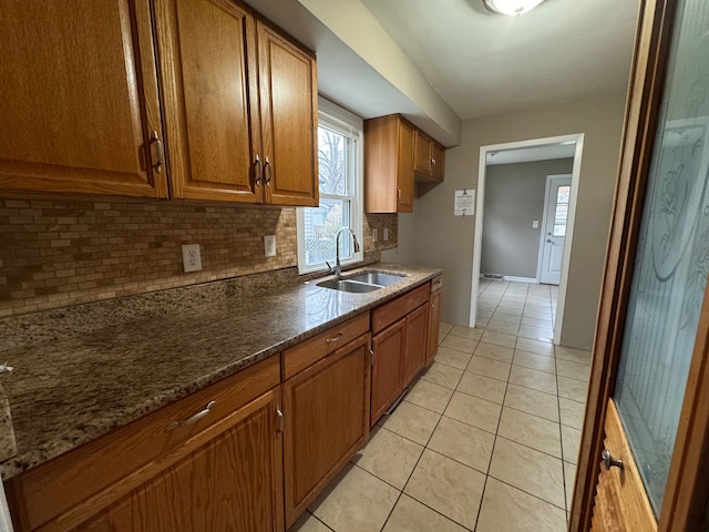 kitchen with dark stone countertops, decorative backsplash, sink, and light tile patterned flooring