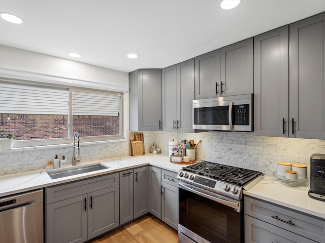 kitchen featuring sink, gray cabinets, decorative backsplash, appliances with stainless steel finishes, and light wood-type flooring