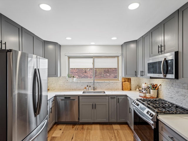 kitchen featuring sink, stainless steel appliances, backsplash, gray cabinets, and light wood-type flooring