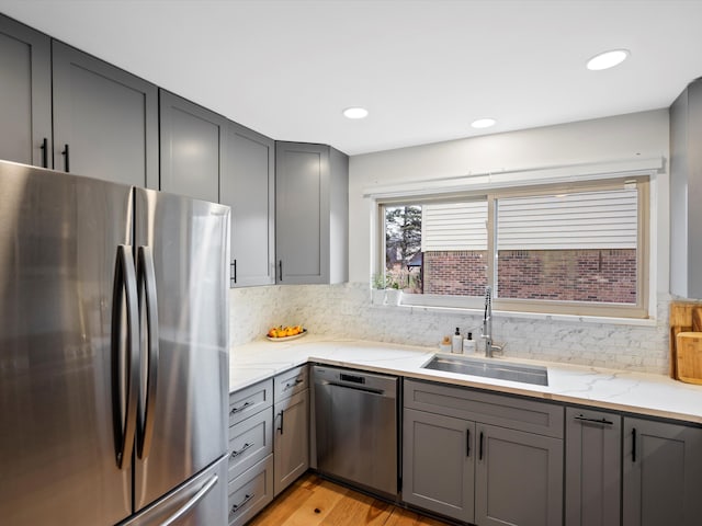 kitchen with sink, gray cabinets, light hardwood / wood-style floors, light stone counters, and stainless steel appliances