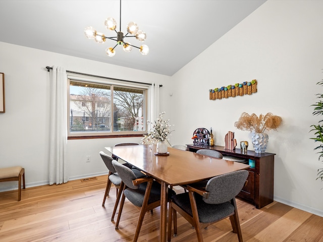 dining area featuring a chandelier, light hardwood / wood-style floors, and vaulted ceiling