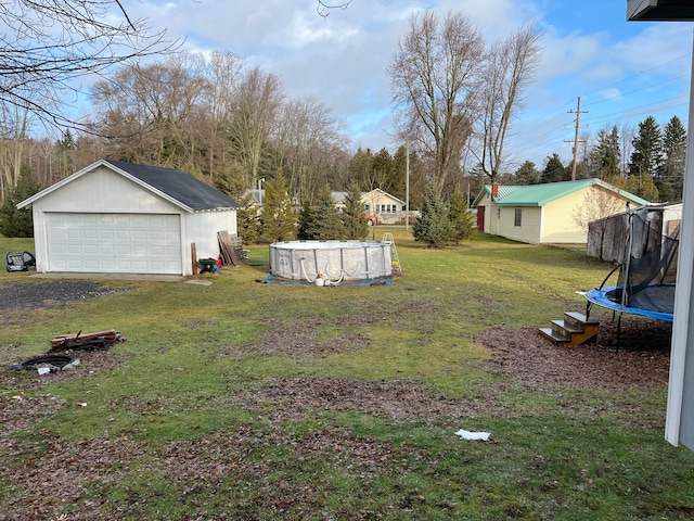 view of yard with an outdoor structure, a garage, a covered pool, and a trampoline