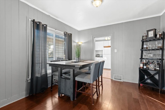 dining area with dark hardwood / wood-style floors, wood walls, and crown molding