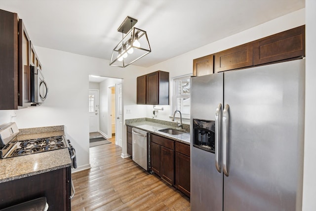 kitchen with sink, light stone counters, light hardwood / wood-style flooring, pendant lighting, and appliances with stainless steel finishes