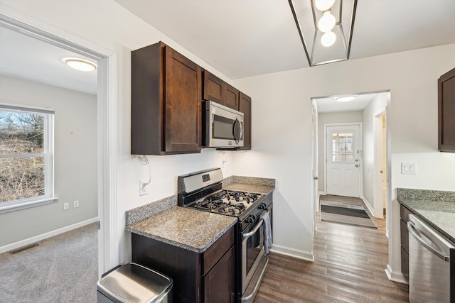 kitchen with dark stone countertops, dark brown cabinets, stainless steel appliances, and dark wood-type flooring