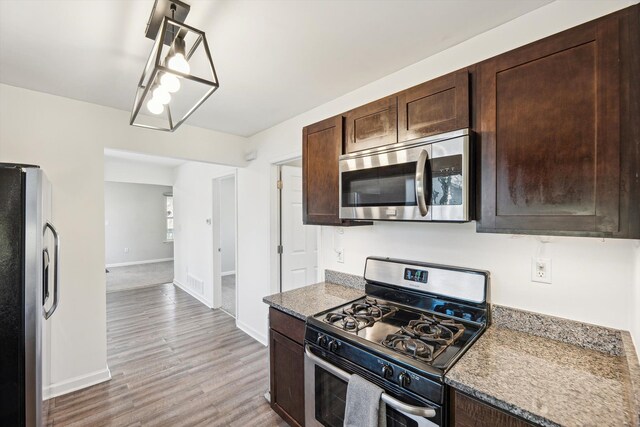 kitchen featuring dark brown cabinetry, stone counters, hanging light fixtures, light hardwood / wood-style flooring, and appliances with stainless steel finishes