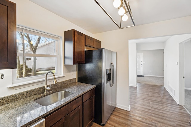 kitchen with sink, light hardwood / wood-style flooring, dark stone countertops, appliances with stainless steel finishes, and dark brown cabinetry