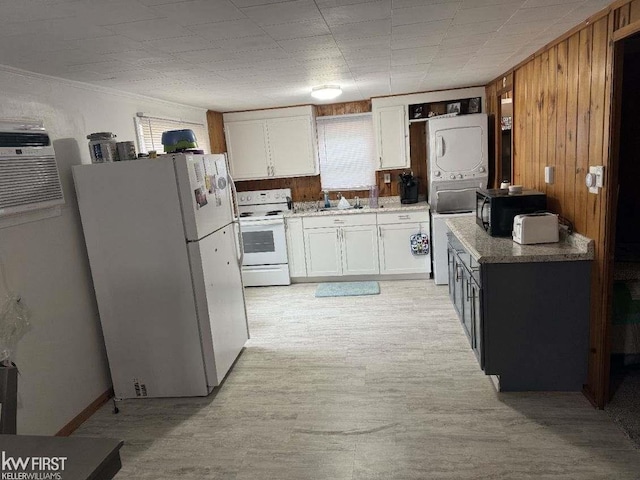 kitchen featuring light stone countertops, white appliances, stacked washer and dryer, white cabinetry, and wood walls