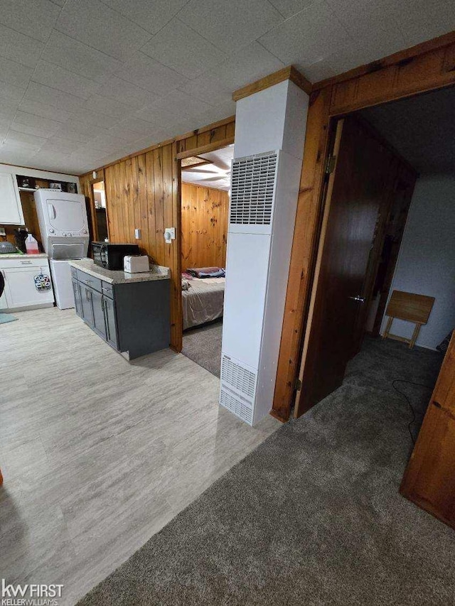 kitchen with stacked washer / drying machine, wood walls, and carpet floors