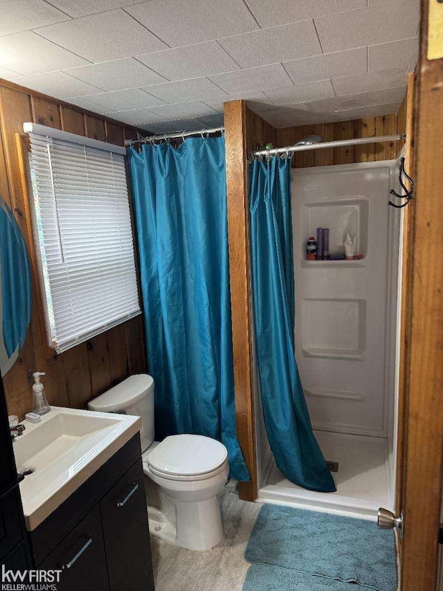 bathroom with a shower with shower curtain, vanity, wood walls, and toilet