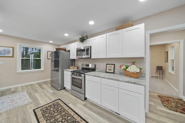 kitchen with white cabinets, appliances with stainless steel finishes, light wood-type flooring, and light stone counters