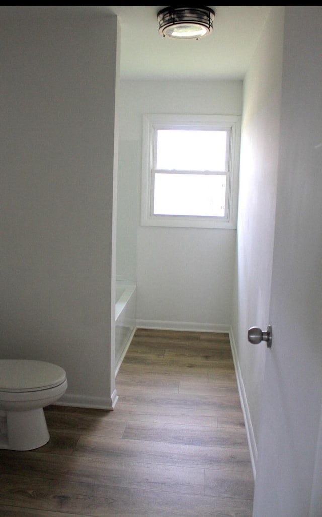 bathroom with a tub to relax in, wood-type flooring, and toilet