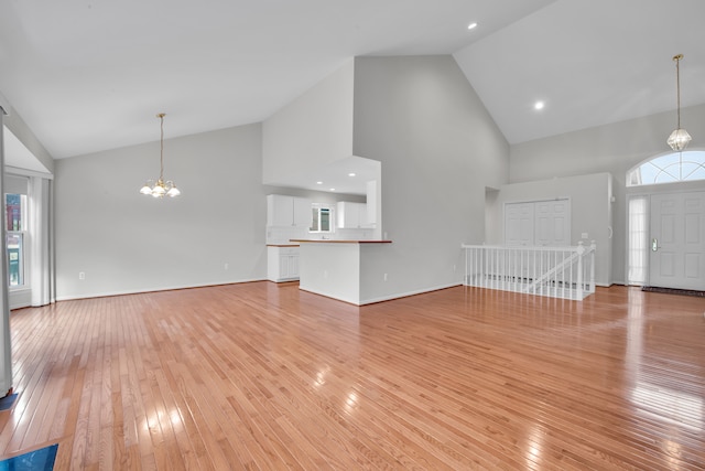 unfurnished living room with high vaulted ceiling, light wood-type flooring, and a notable chandelier