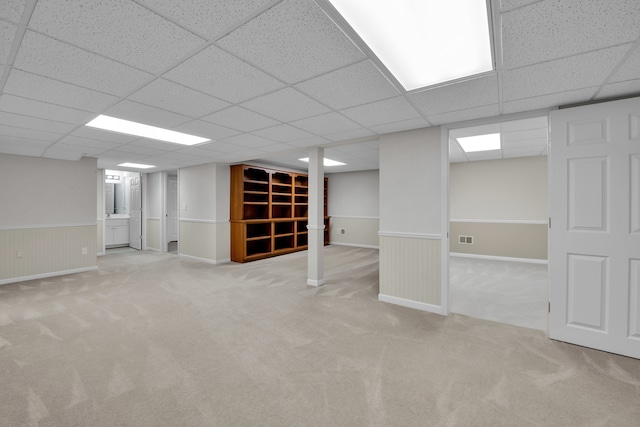 basement featuring a paneled ceiling and light colored carpet