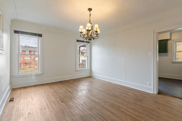 spare room featuring hardwood / wood-style floors, a notable chandelier, a textured ceiling, and a wealth of natural light