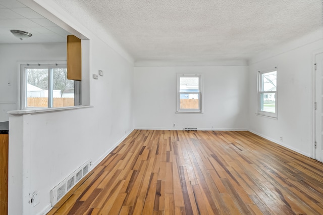 unfurnished room featuring a healthy amount of sunlight, a textured ceiling, and hardwood / wood-style flooring