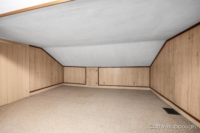 additional living space featuring lofted ceiling, light colored carpet, and wooden walls