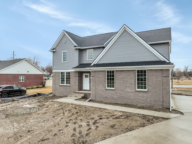 traditional home featuring a shingled roof and brick siding