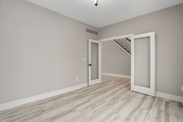 empty room with baseboards, visible vents, stairs, french doors, and light wood-type flooring