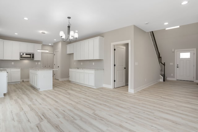 kitchen featuring white cabinetry, baseboards, backsplash, a center island, and stainless steel microwave