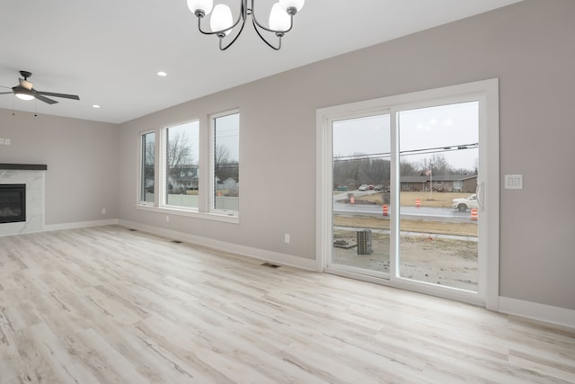 unfurnished living room with recessed lighting, ceiling fan with notable chandelier, a premium fireplace, wood finished floors, and baseboards