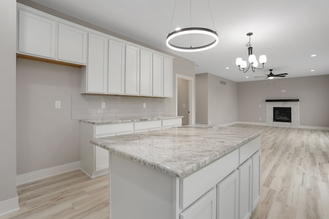 kitchen featuring ceiling fan with notable chandelier, white cabinetry, hanging light fixtures, backsplash, and a glass covered fireplace