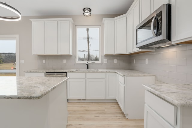 kitchen with tasteful backsplash, stainless steel microwave, light wood-style flooring, a sink, and light stone countertops