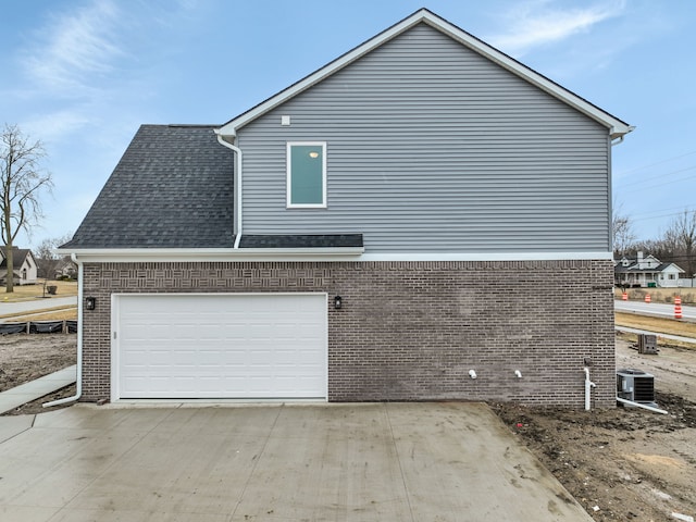 view of side of home featuring a garage, driveway, brick siding, and roof with shingles