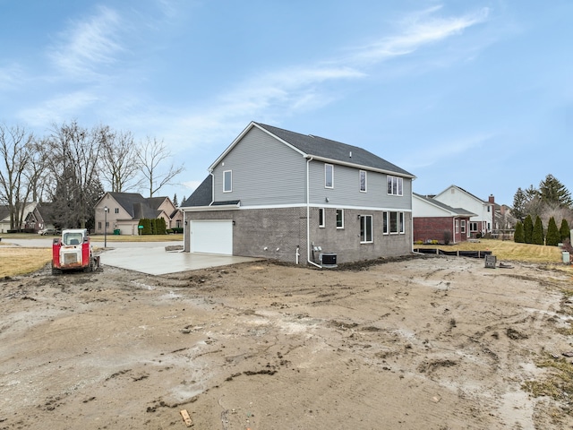 back of house featuring brick siding, driveway, an attached garage, and central AC unit