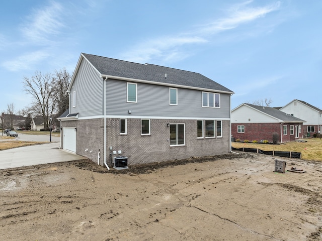 rear view of house featuring a garage, concrete driveway, brick siding, and central AC