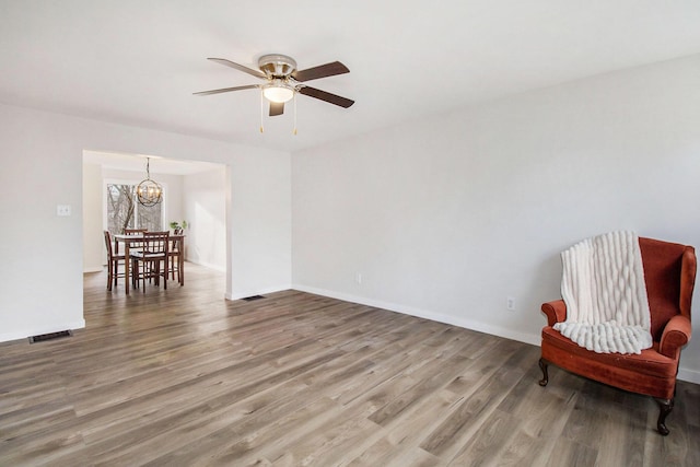 living area featuring ceiling fan with notable chandelier and hardwood / wood-style flooring