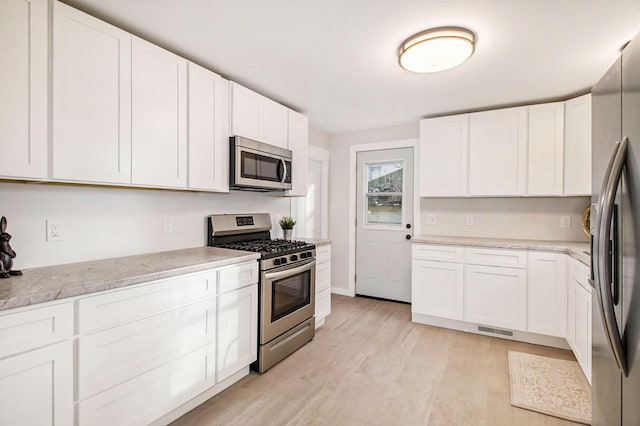 kitchen featuring stainless steel appliances, white cabinetry, light hardwood / wood-style floors, and light stone counters