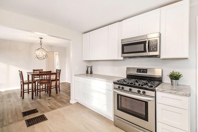 kitchen with stainless steel appliances, a notable chandelier, white cabinets, and light hardwood / wood-style flooring